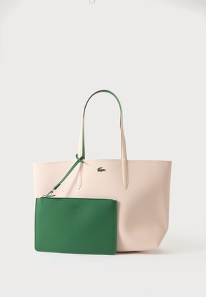 Sac fourre-tout beige avec longues anses et petite pochette zippée verte détachable attachée à une anse, présenté sur un fond uni.
