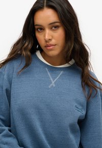 Sudadera azul con un acabado texturizado, con un cuello blanco y detalles en costura contrastantes. Logotipo bordado en el lado izquierdo.