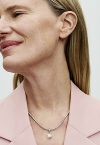 Collana in argento con un pendente a forma di rosa. Il pendente è bianco e la collana presenta un design a trama intrecciata.