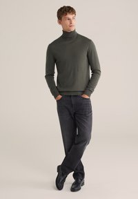 Mörkgrön polotröja i kombination med mörka jeans och svarta skor. Tröjan har en figurnära design, med långa ärmar och en mjuk struktur.