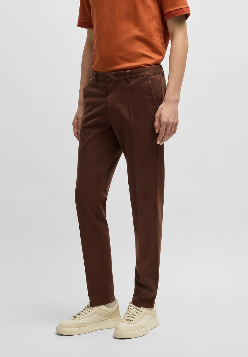 Bruna bomullsbukser med figursydd passform, med sidofickor, bälteshällor och en slät textur, i kombination med krämfärgade sneakers.