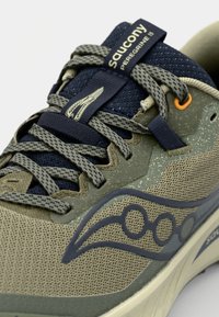 Topánky Saucony Peregrine 15 majú textúrovaný olivovo zelený sieťovinový zvršok, námornícke šnúrky a výrazné logo na boku v tmavomodrej farbe.