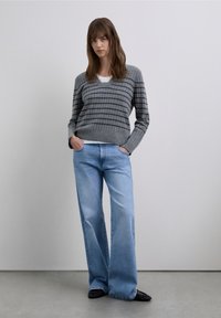 Grå randig tröja med V-ringning, kombinerad med ljusblå jeans med vida ben. Svarta platta skor. Enkel, ren design och mjuka texturer.