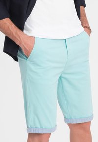 Pantaloni corti di cotone azzurri chiari con parte anteriore piatta, tasche laterali e orli arrotolati con un risvolto a contrasto in azzurro chiaro.