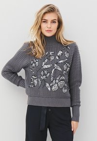 Grijze gebreide trui met geribde col, voorzien van een zilveren pailletten bloemenontwerp op de voorkant, textielstructuur en aansluitende mouwen.
