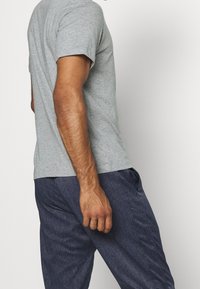 Graues T-Shirt mit kurzen Ärmeln kombiniert mit marineblauen, strukturierten Hosen. Das Shirt hat eine reguläre Passform und eine glatte Stoffoberfläche.