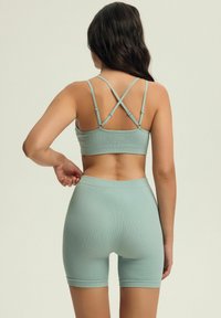 Miętowo-zielony zestaw sportowy z prążkowanej tkaniny składający się z topu na krótki rękaw z krzyżującymi się ramiączkami oraz pasujących szortów z wysokim stanem. Miękka tekstura, dopasowany krój.