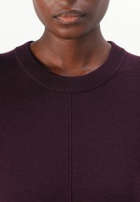 Pull en tricot violet avec un col rond et une texture côtelée, doté d'une couture verticale sur le devant.