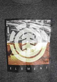 Vierkant grafisch ontwerp op donkere stof met gelaagd cirkelvormig logo over stedelijke en natuurlijke texturen, woord "ELEMENT" eronder in witte letters.