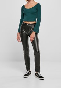 Zelený dlouhý rukáv crop top s kulatým výstřihem, v kombinaci s lesklými černými kalhotami z umělé kůže a černými teniskami s bílou podrážkou.