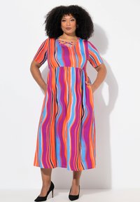 Abito maxi a righe colorato con maniche corte, scollatura a Girocollo con dettagli incrociati e tasche laterali. Il materiale sembra leggero e liscio.