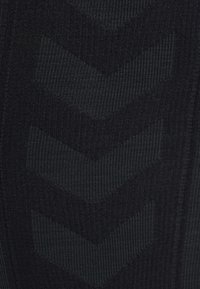 Detailní záběr na tmavou látku s jemným vzorem tří směrů dolů ukazujících šipek v mírně světlejším odstínu.