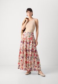 Gonna maxi floreale con design a strati in tessuto rosa chiaro. Presenta motivi di fiori colorati, vita elasticizzata e abbinata a una maglietta beige.