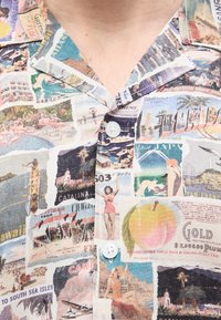 Πουκάμισο με γιακά, με εικονογραφήσεις από vintage ταξιδιωτικές καρτ ποστάλ που απεικονίζουν παραλίες, φοίνικες, κολυμβητές, φλαμίνγκος και ονόματα πόλεων όπως Φλόριντα και Κι Γουέστ.