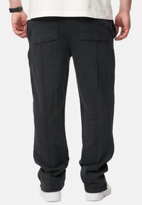 Schwarze Baumwollhose mit relaxtem Schnitt, ausgestattet mit zwei Gesäßtaschen und sichtbaren Nähten, kombiniert mit weißen Sneakers.