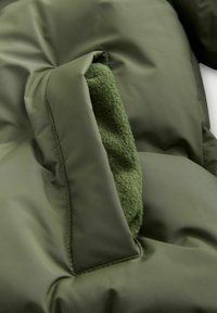 Giacca puffa verde oliva con un interno in morbido pile verde, con un'apertura per la tasca visibile e dettagli cuciti.