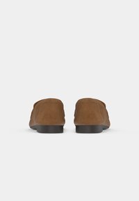 Mocassini in suede marrone con punta tonda e suola nera piatta, caratterizzati da un sottile dettaglio di cucitura sulla parte superiore e da una superficie liscia.