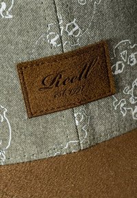 Gray fabric cap featuring a textured brown faux leather patch with "Reell est. 1992" embossed. Pattern of white designs on the fabric.
