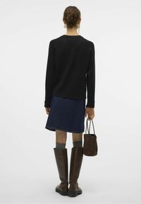 Czarny sweter z dzianiny, dżinsowa spódnica, wysokie brązowe skórzane botki, szare skarpetki oraz mała brązowa torebka. Widok z tyłu na jednolitym tle.