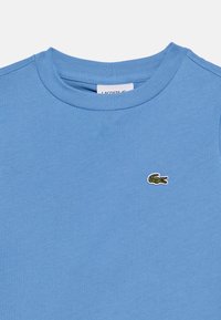 Ανοιχτό μπλε βαμβακερό t-shirt με στρογγυλή λαιμόκοψη και κοντά μανίκια, με μικρό πράσινο κεντητό λογότυπο κροκοδείλου στο στήθος.