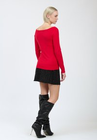 Rode longsleeve top met een wijde halslijn, gecombineerd met een zwart mini-jurkje met streepmotief en zwart leren kniehoge laarzen met hakken.