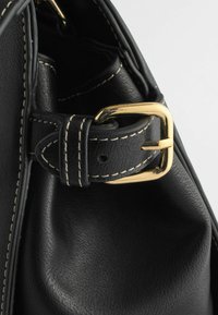 Côté de sac en cuir noir avec coutures blanches et une boucle rectangulaire dorée fixant une boucle de sangle.