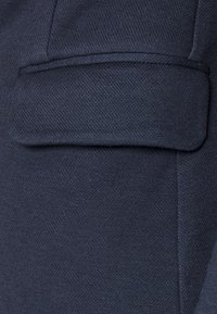 Navy blue fabric with a textured finish, featuring a flap pocket and clean stitching along the edges. The design is simple and practical.