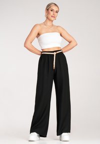 Czarne szerokie spodnie na elastykę z beżowym sznurkiem. W zestawie z białym topem bez ramiączek i białymi butami.