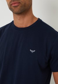 T-shirt a maniche corte blu navy in cotone, caratterizzato da un sottile design ricamato sul petto. Collo a giro e texture morbida.
