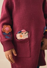 Bordeauxfarbener Strickpullover mit Blumenstickerei an den Ärmeln und einer strukturierten Tasche mit gehäkeltem Tiersdesign.