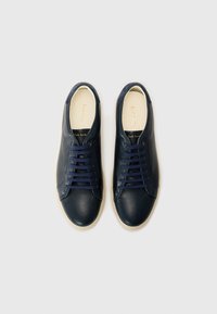 Tumes nahkjalanõud ümarate varvastega, sidumisdisainiga, kreemjas kummitald ja kullakirjaga sisetallal. Sile tekstuur ja voolujooneline kuju.