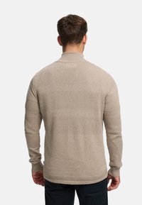 Beige stickad tröja med hög krage och texturerade ränder. Långa ärmar med ribbade muddar och en avslappnad passform.