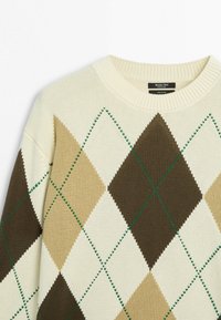 Cremefarbener Strickpullover mit beige-braun-weißem Argyle-Rautenmuster und grünen Ziernähten, Rundhalsausschnitt und einem schwarzen Etikett im Innenkragen.