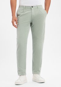 Παντελόνι χειμωνιάτικο βελουτέ ανοιχτοπράσινο με υφή, με πλαϊνές τσέπες, κούμπωμα με κουμπί και στενές μπατζάκια. Φορεμένο με λευκά αθλητικά παπούτσια.