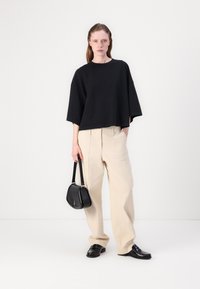 Μαύρο oversized t-shirt, χαλαρή εφαρμογή. Κρέμ παντελόνι με φαρδιά πόδια, υφασμάτινη υφή. Μαύρη τσάντα ώμου με καμπύλη μορφή, αση�μένιες λεπτομέρειες. Μαύρα παπούτσια.