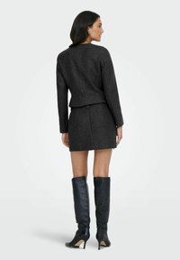 Grå ullblazer med figursydd design och långa ärmar, tillsammans med en matchande minikjol och knähöga svarta läderstiletto stövlar.