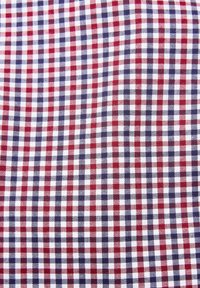 Tejido de cuadros en rojo y azul marino con un patrón a cuadros, que presenta cuadrados espaciados de manera uniforme sobre un fondo blanco. Material de algodón texturizado.