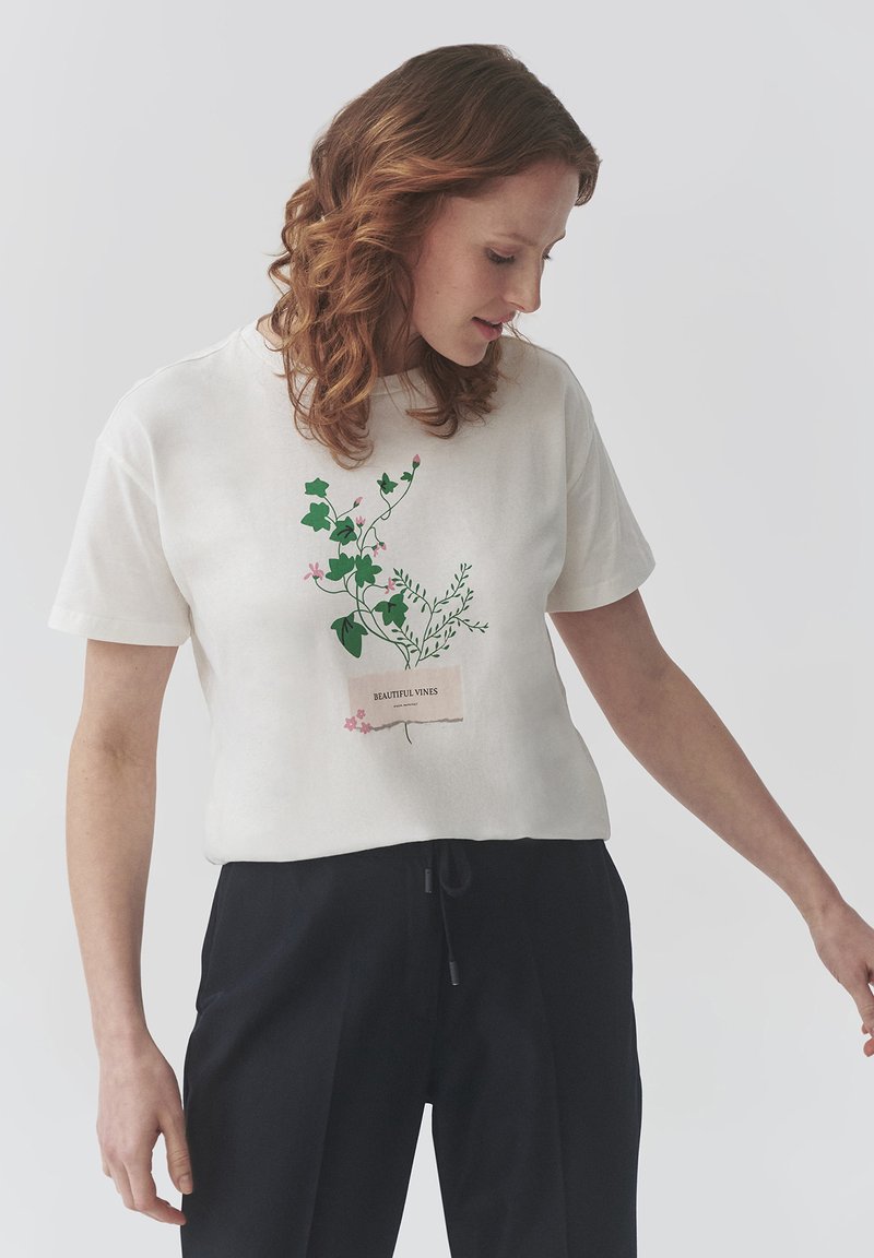 Witte katoenen t-shirt met groene plantgraphics en de tekst "Prachtige Wijnstokken" op een label. Korte mouwen en een losse pasvorm.