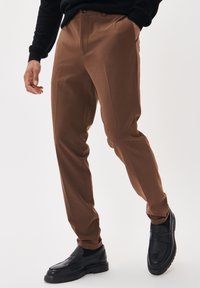 Bruna byxor i texturerat tyg med slim fit, med sidfickor och bärs med svarta loafers.