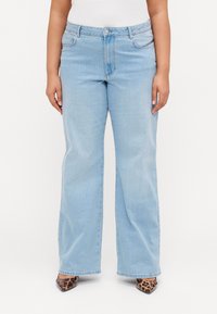 Jeans de perna reta em azul claro, feitos de denim, com bolsos frontais, fecho com botão e um desbotado sutil. Usados com saltos agulha de estampa de leopardo.