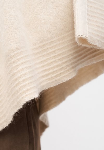 Pull beige en maille avec une texture côtelée et un tissu doux. Les bords sont légèrement effilochés, donnant un aspect léger et aéré.
