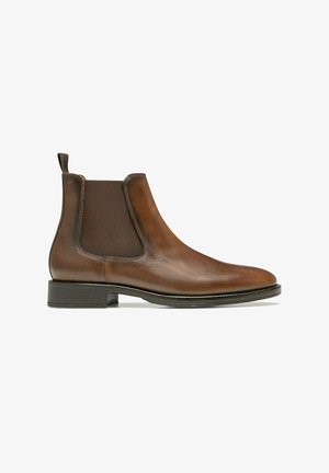 Bottine Chelsea en cuir marron avec des panneaux élastiques sur les côtés, une languette de tirage et une semelle texturée, bout rond et talon bas.