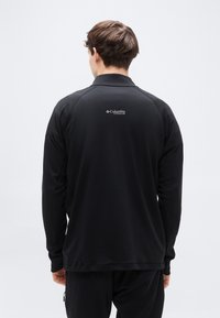 Μαύρο πουκάμισο μακρυμάνικο με γιακά, με υφή στο ύφασμα και το λογότυπο Columbia Titanium στο πάνω μέρος της πλάτης. Απλός σχεδιασμός, χωρίς σχέδια.