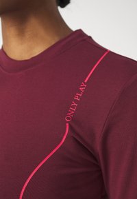 Maglietta sportiva bordeaux con dettaglio testuale rosa "ONLY PLAY". Realizzata in un tessuto morbido e elastico con un design aderente.