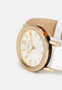 Guld-tone ur med rund urskive, hvid tekstureret skive, guld timer markører, og et hvidt læderrem. Har mærkenavnet "Furla."
