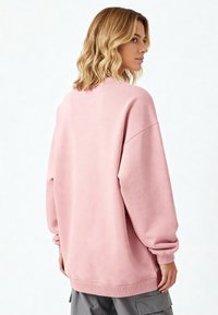 Felpa rosa oversize con una texture morbida, collo tondo e polsini a coste, abbinata a pantaloni cargo grigi.