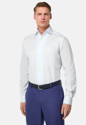 Hellblau gestreiftes Hemd mit spitzem Kragen, langen Ärmeln und Knopfleiste, kombiniert mit einem dunklen Gürtel und lila Hose.