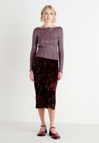 Haut en maille bordeaux à manches longues, en tissu texturé, associé à une jupe moulante en sequins de couleur bourgogne foncé. Mannequin portant des chaussures à talons assorties.