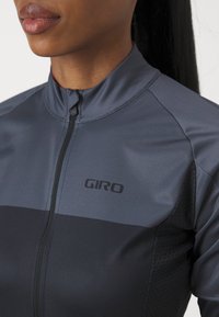 Maillot de cyclisme pour homme en gris foncé avec un col zippé, texture respirante, rayure noire horizontale et logo Giro sur la poitrine.