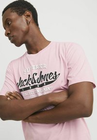 Rosa Baumwoll-T-Shirt mit einem großen weißen und schwarzen Drucklogo. Das Shirt hat kurze Ärmel und ein Rundhalsausschnitt-Design.